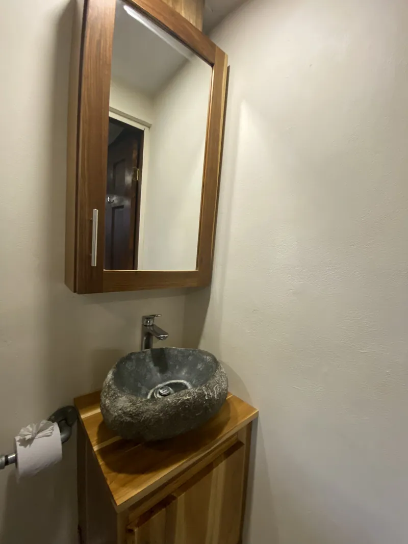 A natural stone vessel sink on a wooden vanity beneath a wood-framed mirror cabinet in the bathroom.