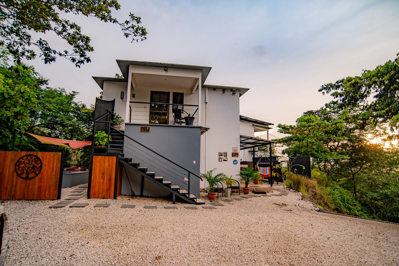 Villa Alegria at dusk — the two-story white villa with its outdoor staircase and gravel courtyard, framed by trees