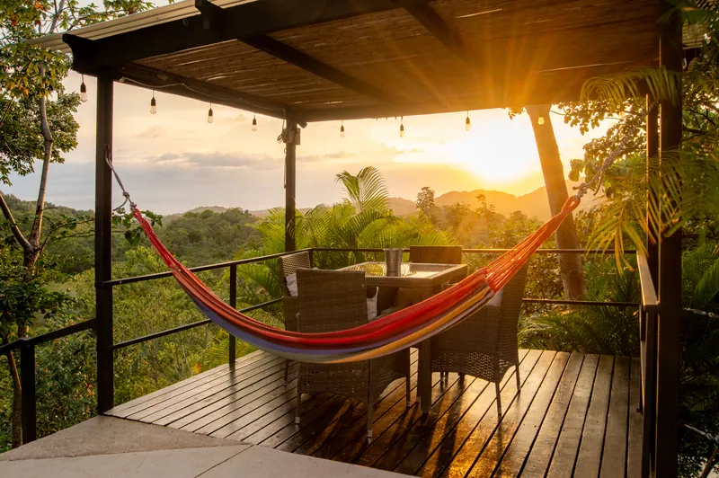 A striped hammock and shaded dining table on the sunset pergola deck, overlooking the jungle hills at Villa Sol